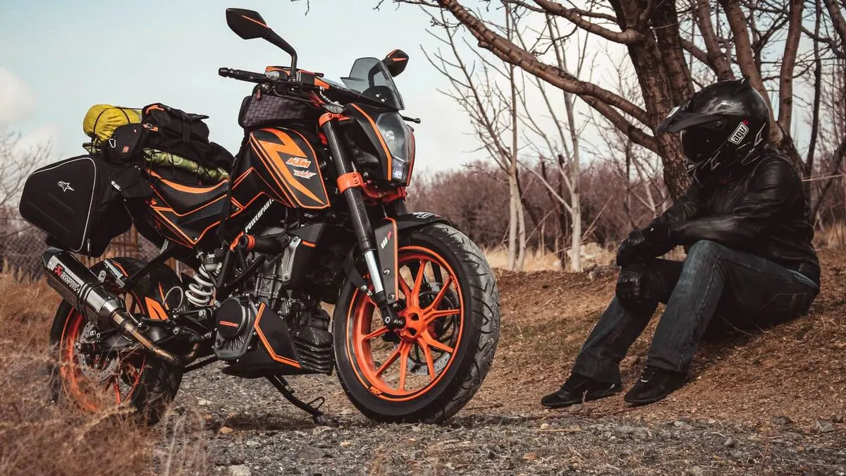 Sacoche de réservoir moto ouverte avec bouteille d'eau, outillage, crème solaire et gants posés sur une selle